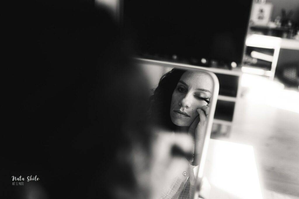 Moment intime : La mariée se maquille devant le miroir en noir et blanc.